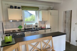 A compact kitchen with a central island, white cabinets, a window with a view, and a rustic wall panel. - Holiday home in Langholz with swimming pool (Langholz)