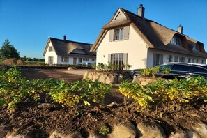 A residential property with a large house featuring a thatched roof, a driveway, and a car parked in the driveway. - Thatched house "Goldmarie" (Zierow)