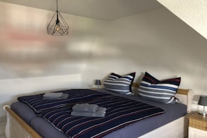 A bedroom with a bed, pillows, a bedside table, and a hanging light fixture. - Thatched house "dat huus" (Zierow)