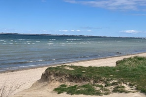 A beach with clear water, a sandy shore, and a distant shoreline. - Thatched house "dat huus" (Zierow)