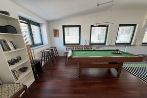 Ein Zimmer mit Poolbillard, Bücherregal und einem Fenster mit Jalousien.