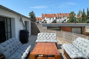 Eine Dachterrasse mit einem Holztisch, zwei Sofas und einer schwarzen Tasche.