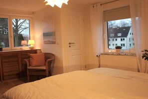 A bedroom with a bed, a chair, a desk, a window with curtains, and a radiator. - Holiday home "Mittenmang" (Schleswig)