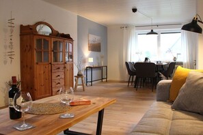 En stue med et træskab, et spisebord med stole, en sofa med pude og et vindue med gardiner.
