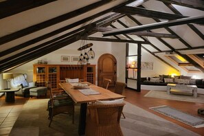An attic room with exposed wooden beams, a dining table with chairs, a sofa, and a fireplace. - Exclusive holiday apartment with views of the Harz Mountains (Goslar)