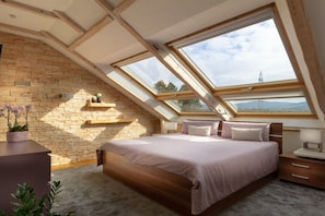 A bedroom with a sloped ceiling, skylights, a bed, bedside tables, and a stone wall. - Exclusive holiday apartment with views of the Harz Mountains (Goslar)