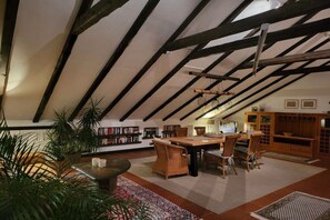 Une pièce mansardée avec des poutres apparentes, une table à manger avec des chaises, une bibliothèque et un buffet.