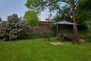 A patio with a table and chairs, a stone wall, and a tree. - Holiday apartment with 2 bedrooms (Panker\/ Gadendorf)