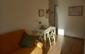 Ein gemütliches Wohnzimmer mit einer Couch, einem kleinen Tisch und einem Sessel. Auf dem Tisch steht eine Lampe und an der Wand hängt ein Kalender.