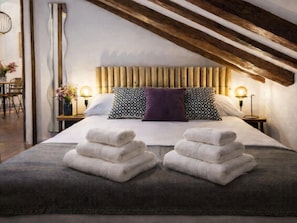 Ein Schlafzimmer mit Holzboden, einem Bett mit weißer Bettwäsche, zwei Kissen und einem Nachttisch mit Lampe.