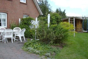 A brick house with a patio area featuring white plastic chairs and a small garden with various plants. - Holiday apartment with 2 bedrooms (Klixbüll)