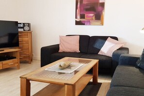 A living room with a sofa, a coffee table, a television, and a cabinet with a radio. - Andreas-Dirks-Straße 1 (Westerland)