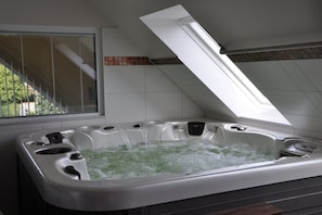 Een jacuzzi met dakraam, gelegen in een ruimte met witte betegelde muren en een raam.