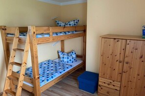Ein Stockbett mit einer Leiter, einer blauen Matratze mit Punkten und einem Holzkasten.