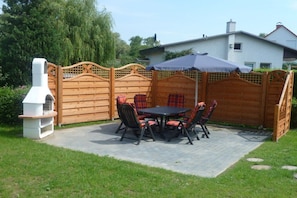 Een terras buiten met een houten omheining, een barbecue en een tafel met stoelen.
