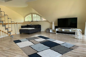 Ein Wohnzimmer mit einer Couch, einem Flachbildfernseher, einer Treppe und einem großen Fenster.