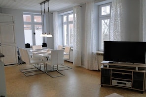 A modern living room with a flat-screen TV, a dining table with chairs, and large windows with curtains. - Holiday apartment with 2 bedrooms (Kappeln Stadt)
