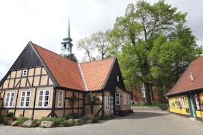 A traditional half-timbered building with a red-tiled roof, a church steeple in the background, and a paved courtyard. - Holiday apartment with 2 bedrooms (Kappeln Stadt)