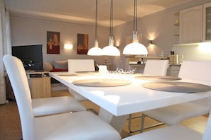A modern dining area with a white table, multiple chairs, and pendant lighting. - Holiday apartment with 2 bedrooms (Kappeln Stadt)