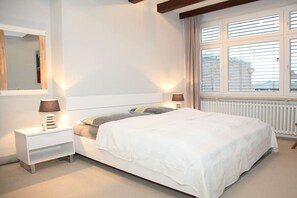 Une chambre à coucher avec un lit, des tables de chevet, un miroir et une fenêtre avec des stores.