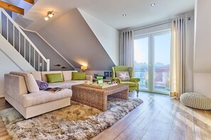 Ein modernes Wohnzimmer mit einer Couch, einem Sessel und einem Couchtisch, einer Treppe und einer großen Schiebeglastür, die auf einen Balkon führt.