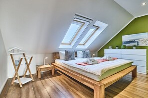 Ein Schlafzimmer mit Schräge, Dachfenstern, einem Bett, Nachttischen und einer Kommode.