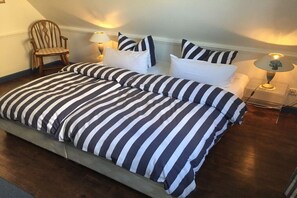 A bedroom with a large bed, two bedside tables with lamps, a wooden chair, and a sloped ceiling. - Elvi Fox House||Sylt (Sylt \/ Westerland)