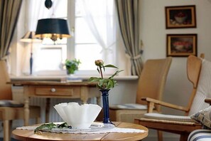 A room with a round wooden table, a blue vase with a single flower, a white decorative bowl, and a chair with a cushion. - Elvi Fox House||Sylt (Sylt \/ Westerland)