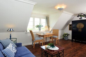 A room with a sloped ceiling, a dining table with chairs, a sofa, a small table with a plant, and a cabinet with decorative items. - Elvi Fox House||Sylt (Sylt \/ Westerland)