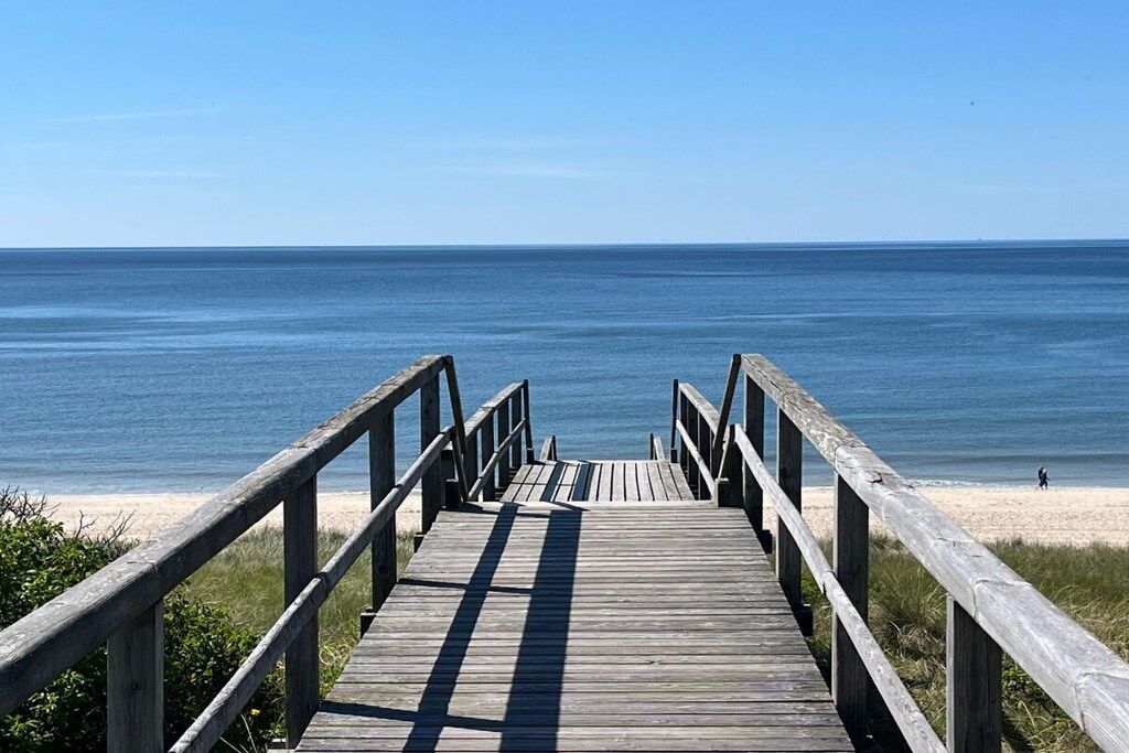 A wooden boardwalk leading to a beach with a clear view of the ocean.