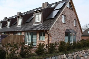 Ein zweigeschossiges Haus mit geneigtem Dach, zahlreichen Fenstern und einem Holzzaun.