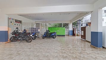A covered parking area with a tiled floor, a green storage unit, and a control panel with emergency lights.