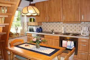 A kitchen with wooden cabinets, a dining table with a placemat, a vase with flowers, and a hanging light fixture. - Holiday apartment in Schneverdingen with Wi-Fi (Schneverdingen)