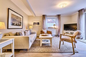 A living room with a sofa, a coffee table, a television, and a chair. - Stylish 3-room holiday apartment "City Oasis" (Westerland)
