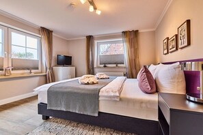 A hotel room with a bed, bedside table, TV, window with curtains, and artwork on the wall. - Stylish 3-room holiday apartment "City Oasis" (Westerland)