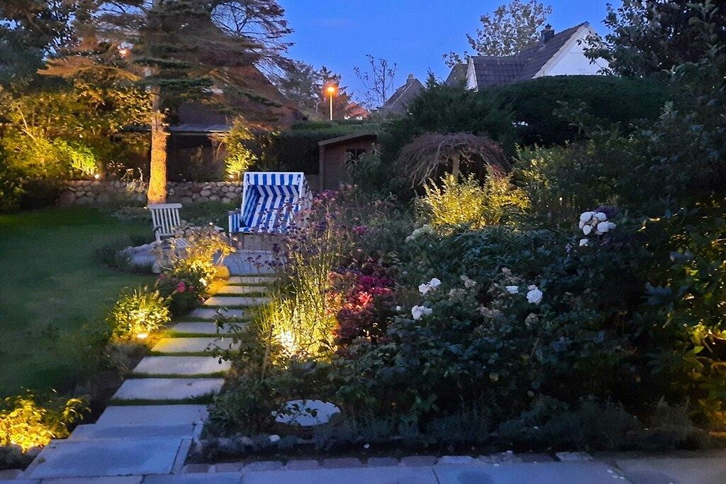 Un sentier de jardin qui mène à une maison avec un petit abri de jardin et un banc.