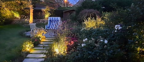 A garden pathway leading to a house with a small shed and a bench.