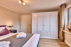 A hotel room with a bed, a wardrobe, a nightstand, and a window with curtains. - Stylish 3-room holiday apartment "City Oasis" (Westerland)