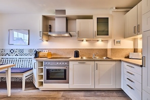 A compact kitchen with a built-in oven, a stove, and a sink. There is a bench with a cushion, and the walls are adorned with patterned tiles. - Stylish 3-room holiday apartment "City Oasis" (Westerland)