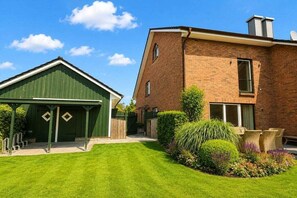 A residential property with a green garage, a brick house, and a well-maintained lawn. - Holiday home in Gelting with swimming pool (Gelting)