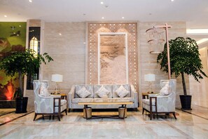 A lobby with a sofa set, two armchairs, a coffee table, a decorative wall panel, and a chandelier.