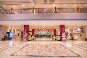A hotel lobby with a marble floor, reception desk, seating area, vending machines, and a balcony. - ningbohangzhouwanhaidiwenquanjiudian (Ningbo)