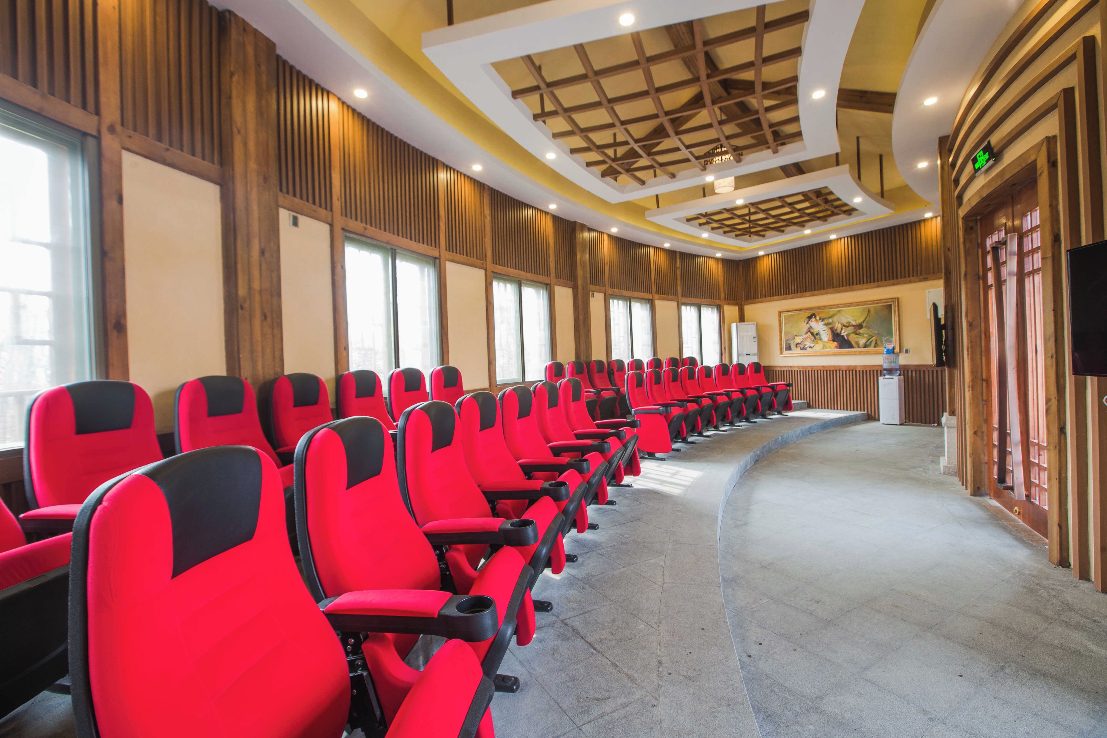 A row of red chairs in a conference room with wooden paneling and a ceiling with recessed lighting.
