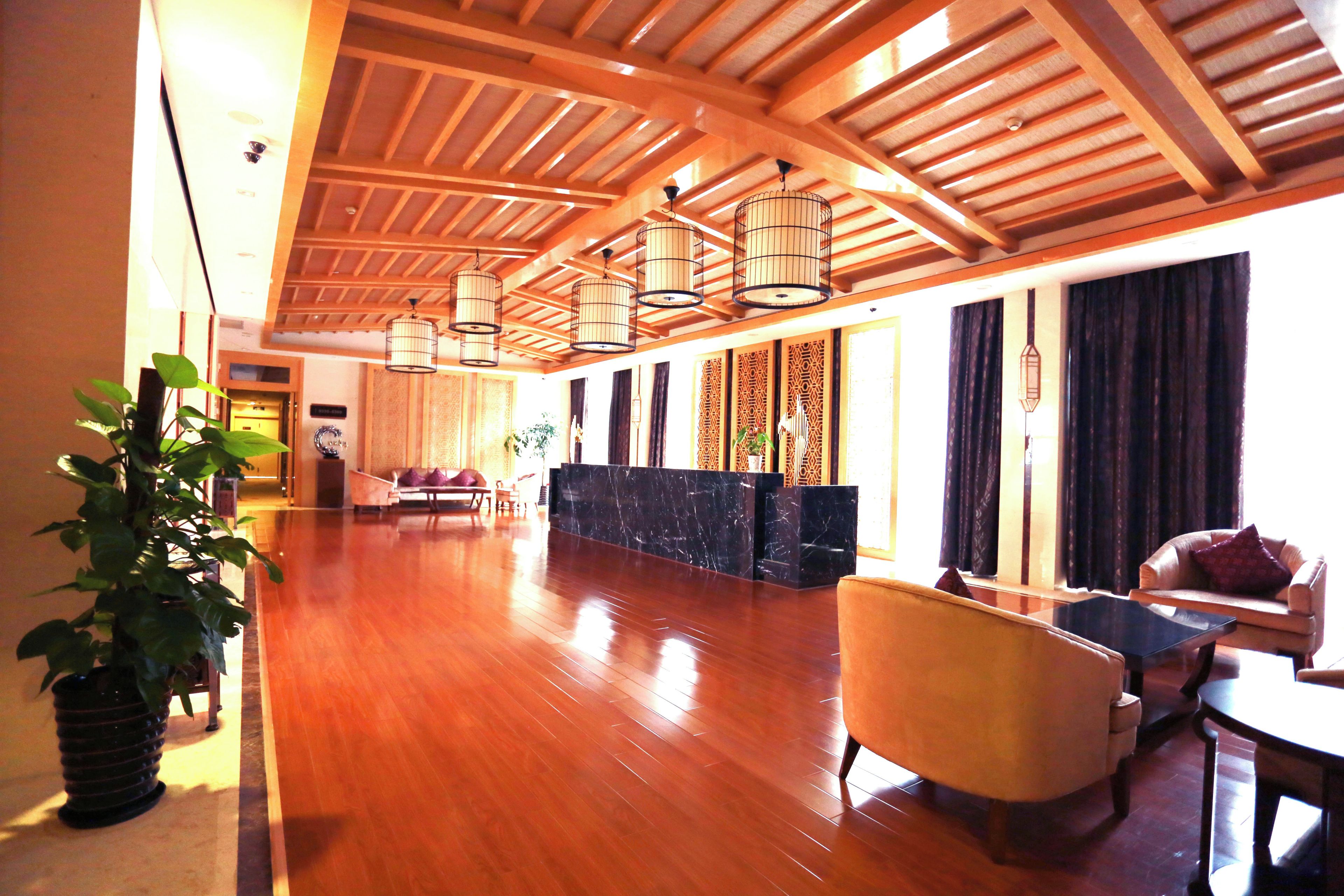 A spacious lobby with a wooden ceiling, a reception desk, seating area, and a large potted plant.