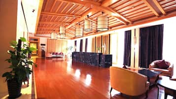 A spacious lobby with a wooden ceiling, a reception desk, seating area, and a large potted plant.