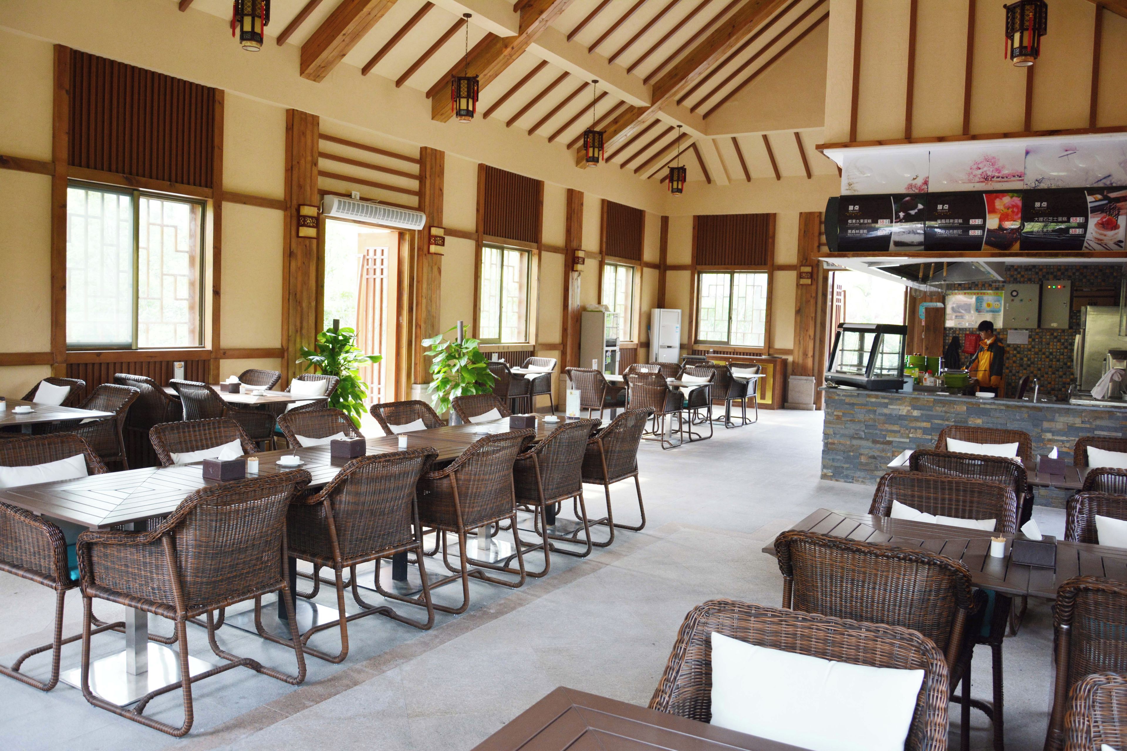 A spacious indoor dining area with high ceilings and wooden beams, featuring multiple tables and wicker chairs.