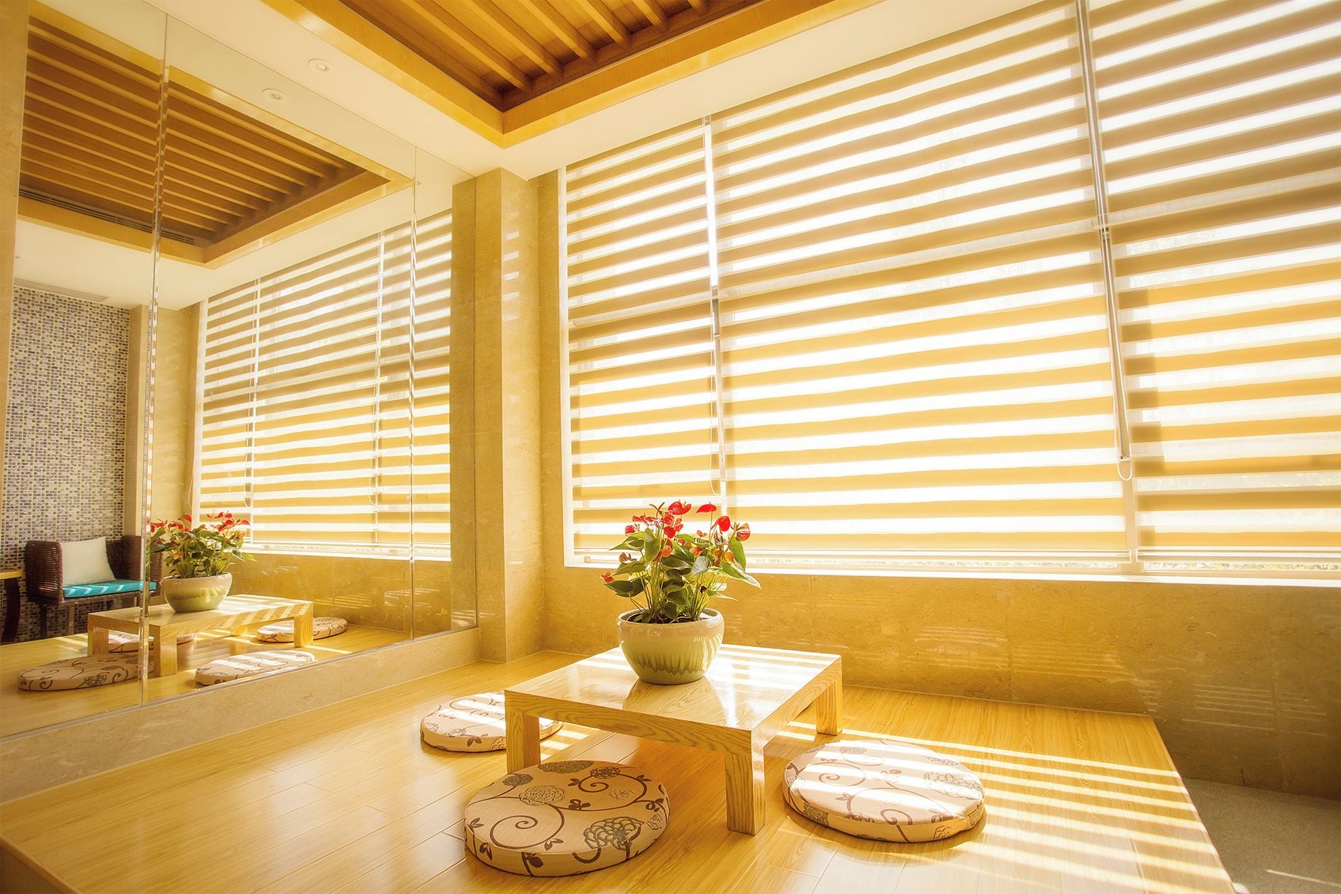Una habitación con piso de madera, un sofá, una mesa y un ventanal con persianas horizontales.