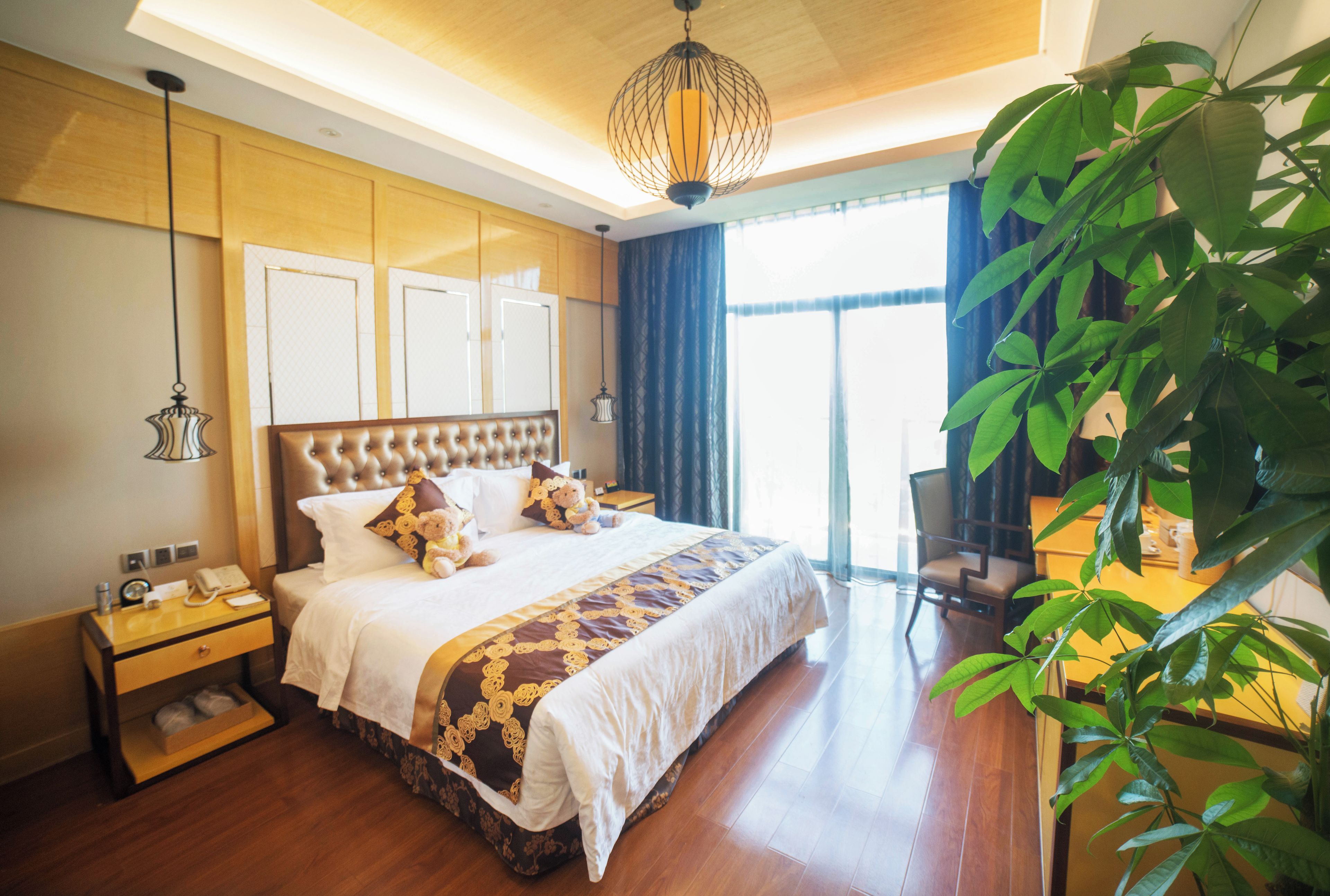 A hotel room with a large bed, a bedside table, a lamp, and a view of the outdoors.