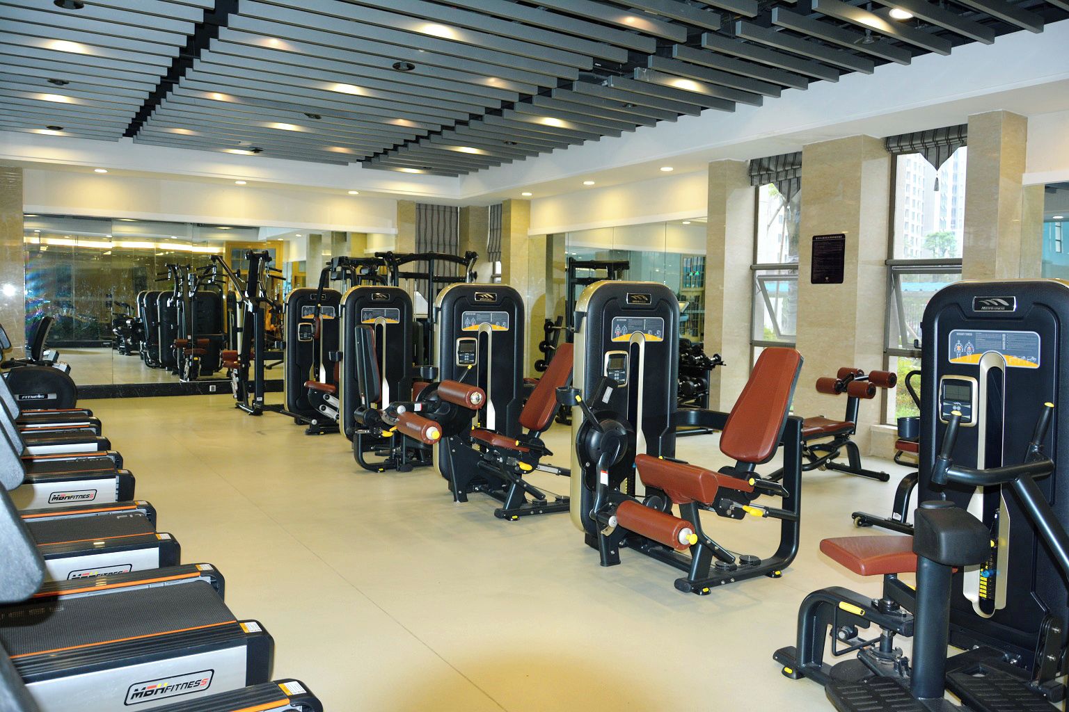 Un gimnasio con diversas máquinas de ejercicio, incluyendo cintas de correr y estaciones de pesas, dispuestas en filas.