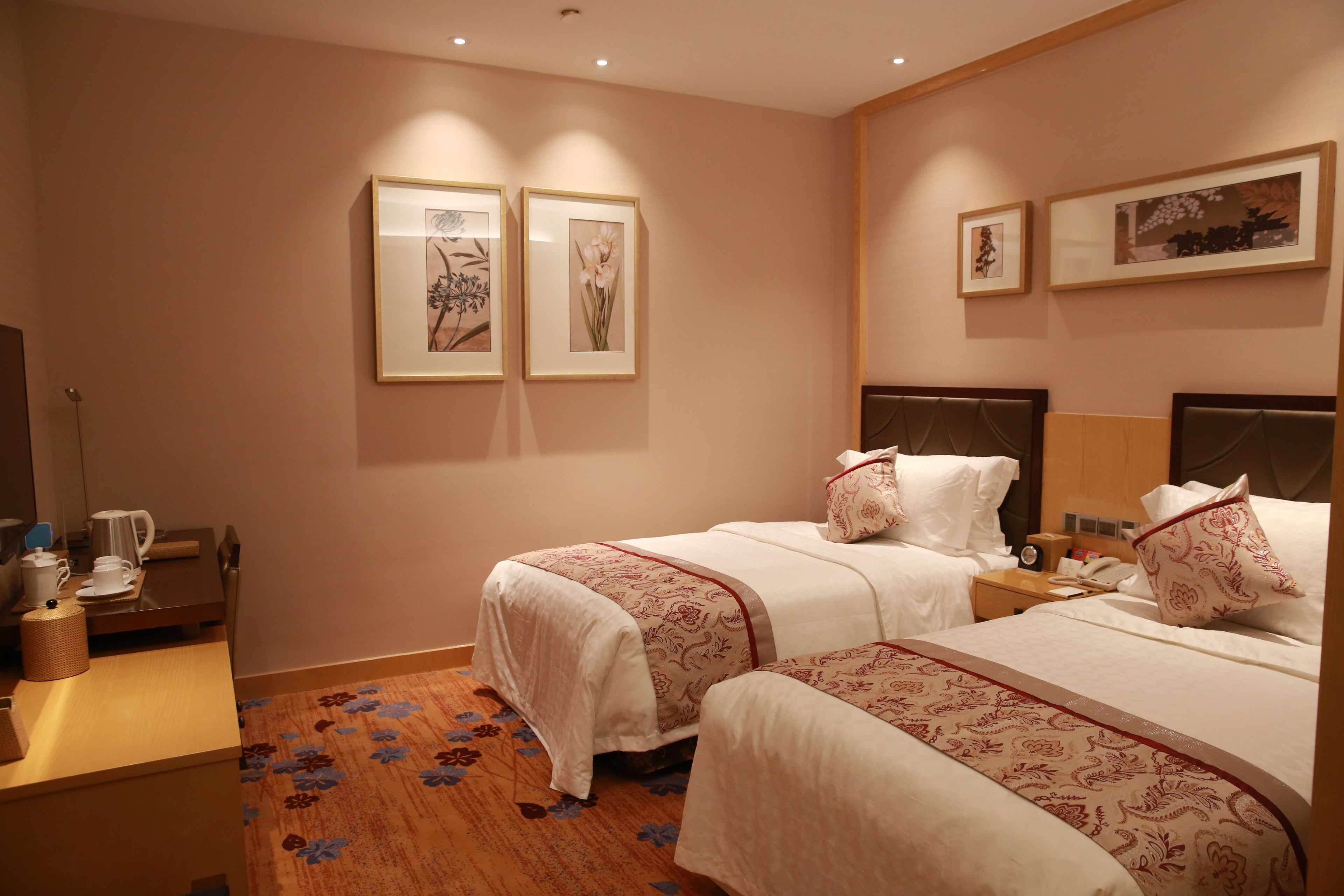 A hotel room with two beds, a desk with a coffee maker, and framed pictures on the wall.